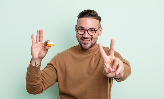 Homem jovem bonito sorrindo e parecendo amigável, mostrando o número dois. lentes de contato