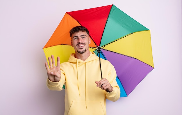 Homem jovem bonito sorrindo e parecendo amigável, mostrando o número quatro. conceito de guarda-chuva