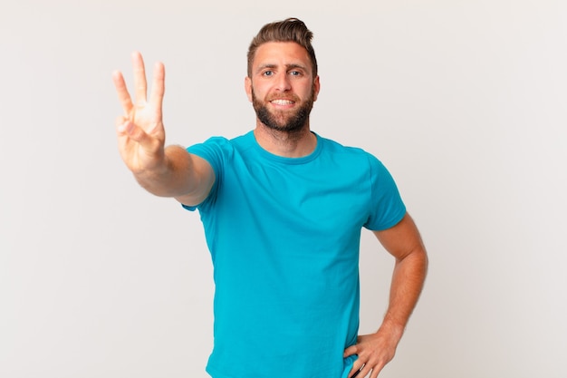 Homem jovem bonito sorrindo e parecendo amigável, mostrando o número três. conceito de fitness