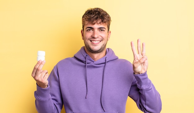 Homem jovem bonito sorrindo e parecendo amigável, mostrando o número três. conceito de frasco de comprimidos