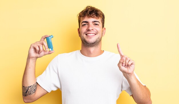 Homem jovem bonito sorrindo e parecendo amigável, mostrando o número um. conceito de asma