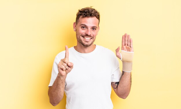 Homem jovem bonito sorrindo e parecendo amigável, mostrando o número um. conceito de bandagem de mão