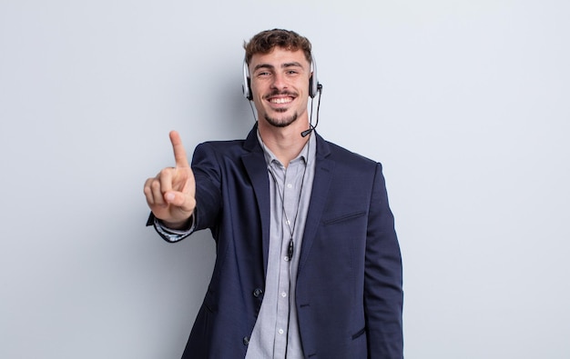 Homem jovem bonito sorrindo e parecendo amigável, mostrando o número um. conceito de telemarketing