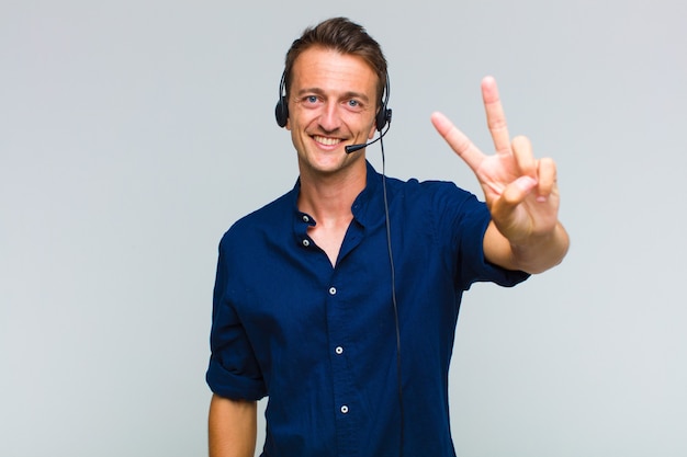 Homem jovem bonito sorrindo e parecendo feliz, despreocupado e positivo, gesticulando vitória ou paz com uma mão