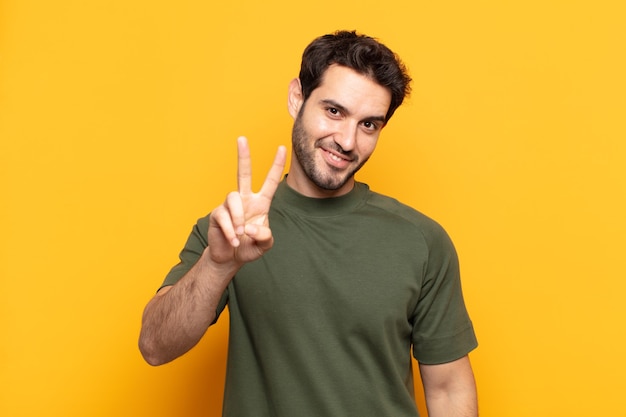 Homem jovem bonito sorrindo e parecendo feliz, despreocupado e positivo, gesticulando vitória ou paz com uma mão