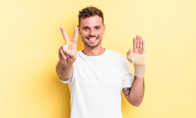 Homem jovem bonito sorrindo e parecendo feliz, gesticulando vitória ou paz. conceito de bandagem de mão