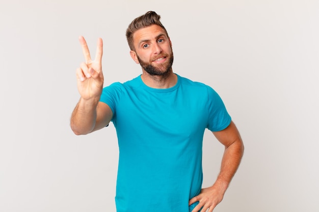 Homem jovem bonito sorrindo e parecendo feliz, gesticulando vitória ou paz. conceito de fitness