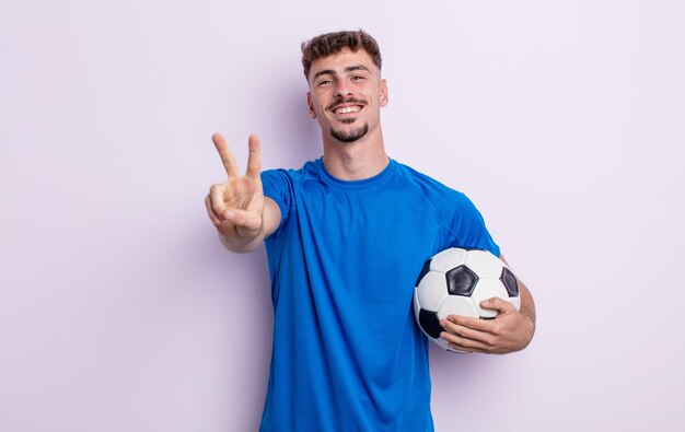 Homem jovem bonito sorrindo e parecendo feliz, gesticulando vitória ou paz. conceito de futebol