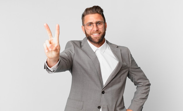 Homem jovem bonito sorrindo e parecendo feliz, gesticulando vitória ou paz. conceito de negócios