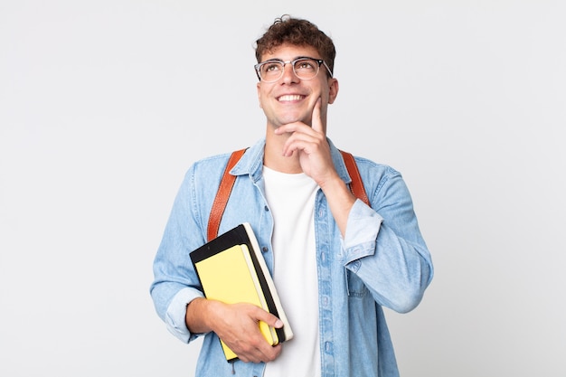 Homem jovem bonito sorrindo feliz e sonhando acordado ou duvidando. conceito de estudante universitário