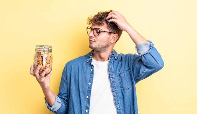 Homem jovem bonito sorrindo feliz e sonhando acordado ou duvidando. conceito de garrafa de biscoitos