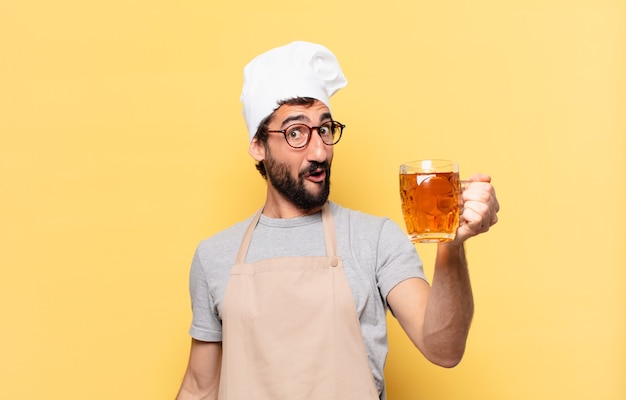 Homem jovem chef barbudo com expressão de surpresa e segurando uma cerveja