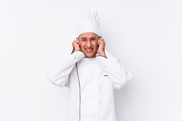 Homem jovem chef latino isolado cobrindo as orelhas com as mãos.