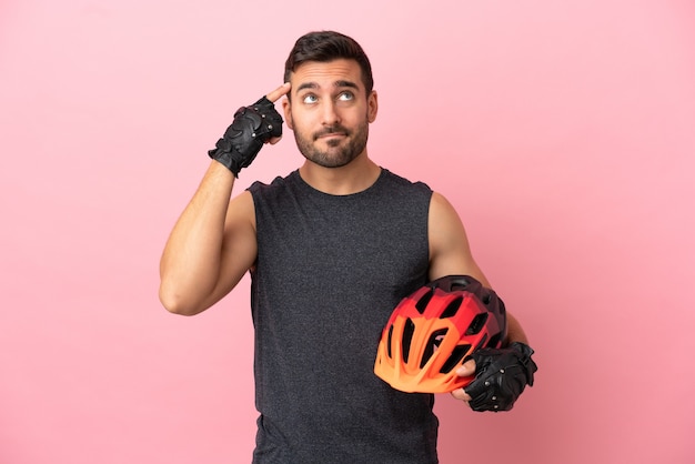 Foto homem jovem ciclista isolado em um fundo rosa, tendo dúvidas e pensando