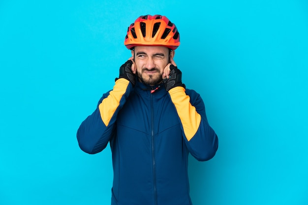 Homem jovem ciclista isolado na parede azul frustrado e cobrindo as orelhas