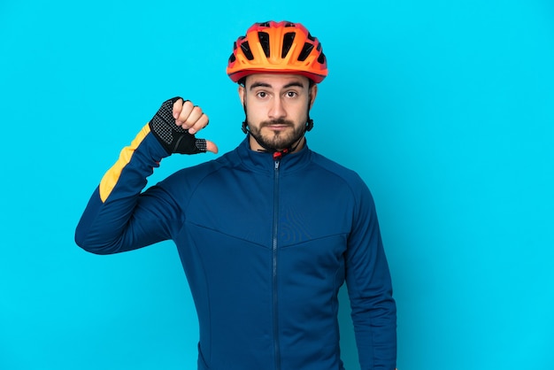 Homem jovem ciclista isolado na superfície azul mostrando o polegar para baixo com expressão negativa