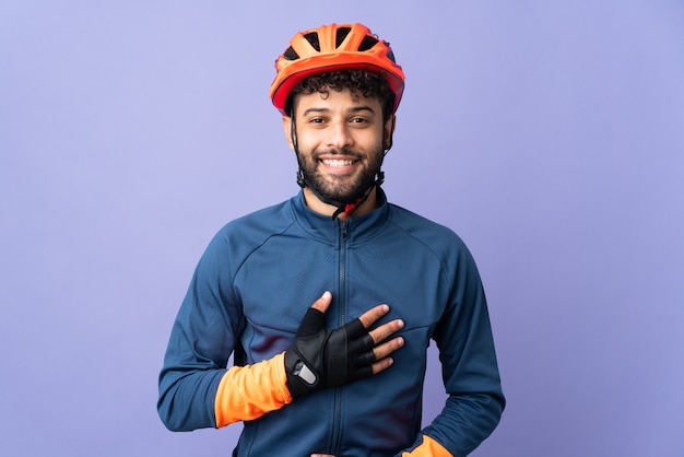 Homem jovem ciclista marroquino isolado em roxo sorrindo muito