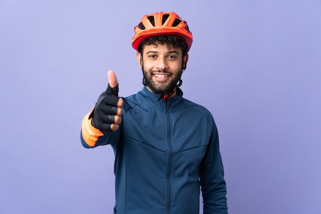 Homem jovem ciclista marroquino isolado na parede roxa com o polegar levantado porque algo bom aconteceu