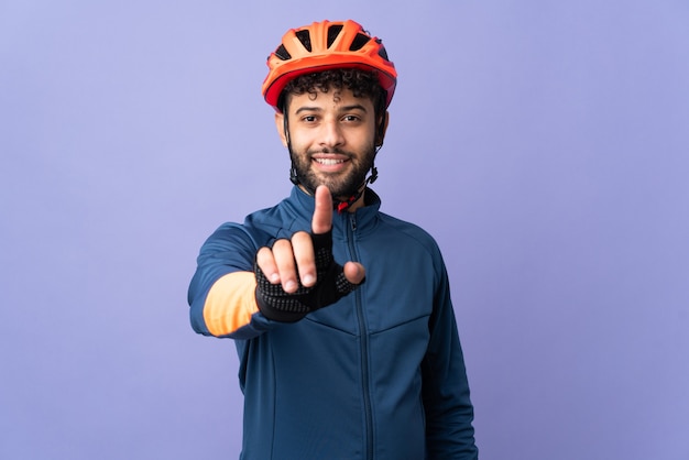 Homem jovem ciclista marroquino isolado na parede roxa, mostrando e levantando um dedo