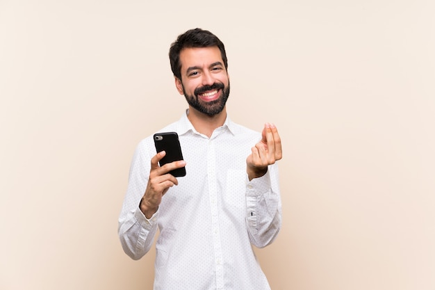 Homem jovem, com, barba, segurando, um, móvel, fazendo, dinheiro, gesto