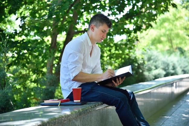 Homem jovem comerciante sentado no parque e analisa relatório de estoque