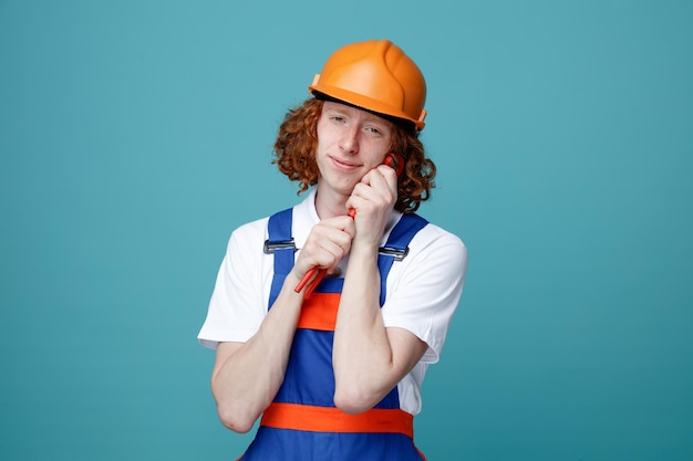 Homem jovem construtor satisfeito em uniforme segurando chave de gás isolada em fundo azul