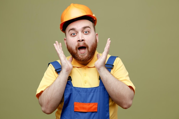 homem jovem construtor surpreso de uniforme isolado em fundo verde