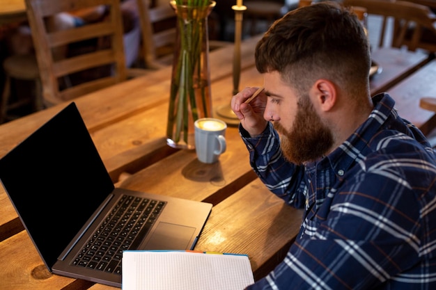 Homem jovem conversando via netbook durante o intervalo do trabalho em uma cafeteria, homem sentado em frente ao laptop aberto com a tela de cópia em branco para sua mensagem de texto ou conteúdo de publicidade