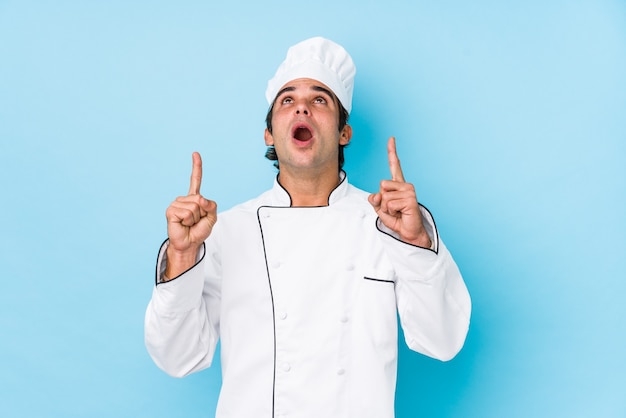 Foto homem jovem cozinheiro isolado apontando para cima com a boca aberta.