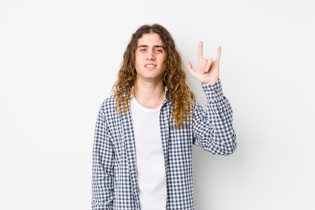 Foto homem jovem de cabelo comprido posando isolado, mostrando um gesto de chifres como um conceito de revolução.