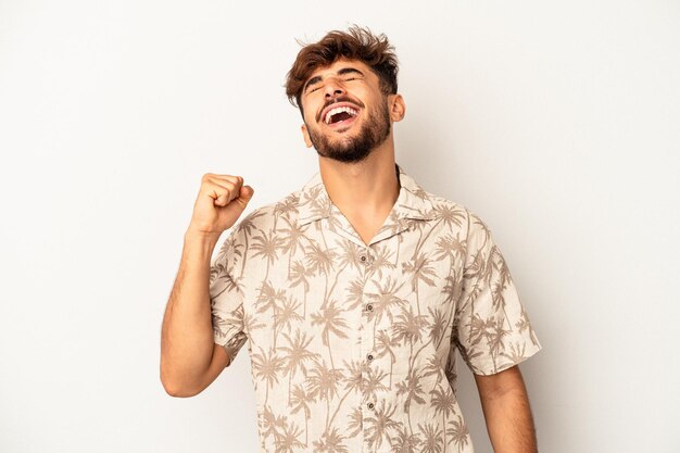 Homem jovem de raça mista isolado em fundo cinza, comemorando uma vitória, paixão e entusiasmo, expressão feliz.