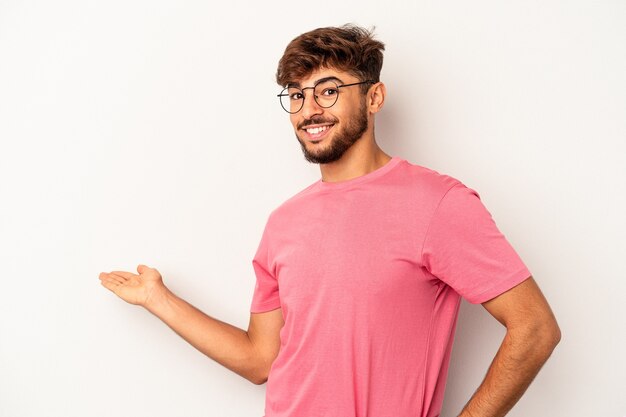 Homem jovem de raça mista isolado em fundo cinza, mostrando uma expressão de boas-vindas.