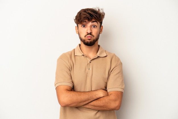 Homem jovem de raça mista isolado em fundo cinza sopra nas bochechas, tem expressão cansada. Conceito de expressão facial.