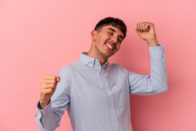 Homem jovem de raça mista isolado em fundo rosa comemorando um dia especial salta e levanta os braços com energia