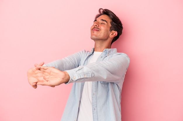 Homem jovem de raça mista isolado no fundo branco, esticando os braços, posição relaxada.