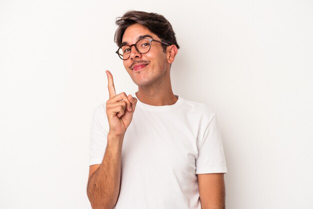 Homem jovem de raça mista isolado no fundo branco, mostrando o número um com o dedo.