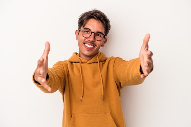 Homem jovem de raça mista isolado no fundo branco, mostrando uma expressão de boas-vindas.