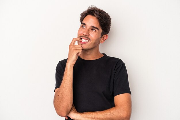 Homem jovem de raça mista isolado no fundo branco relaxado pensando em algo olhando para um espaço de cópia.