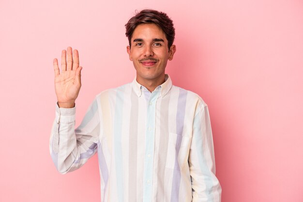 Homem jovem de raça mista, isolado no fundo branco, sorrindo alegre mostrando o número cinco com os dedos.