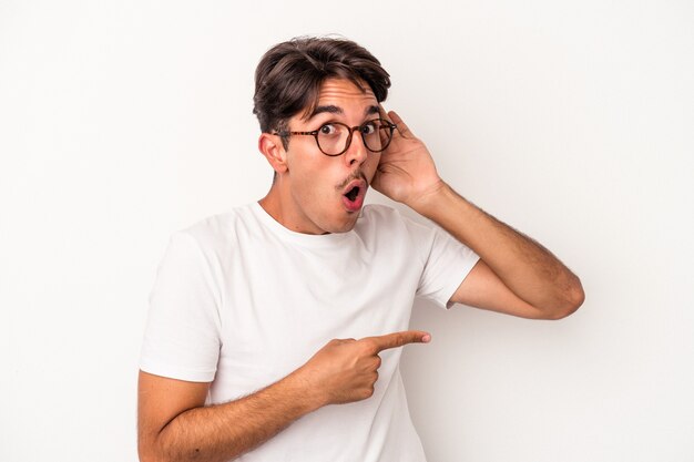 Homem jovem de raça mista, isolado no fundo branco, tentando ouvir uma fofoca.