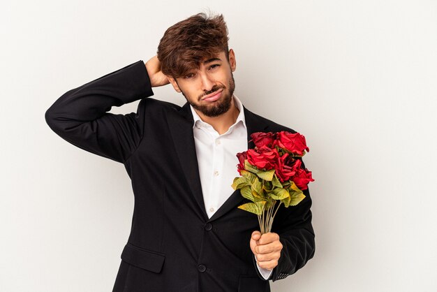 Homem jovem de raça mista segurando buquê de rosas isolado no fundo branco, sendo chocado, ela se lembrou de uma reunião importante.