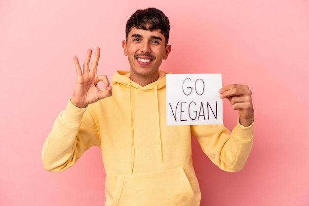 Homem jovem de raça mista, segurando um cartaz vegano isolado no fundo rosa