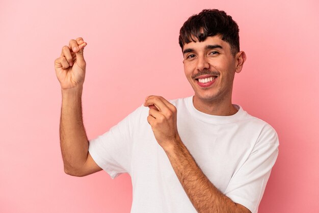 Homem jovem de raça mista segurando um fio dental isolado no fundo rosa