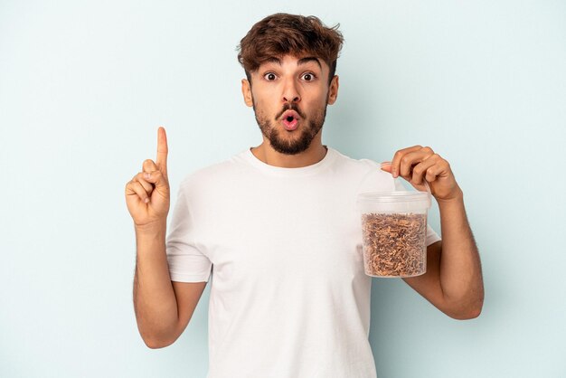 Homem jovem de raça mista segurando uma comida de pássaros isolada sobre fundo azul, tendo uma ótima ideia, o conceito de criatividade.