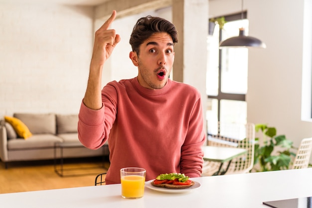 Homem jovem de raça mista tomando café da manhã em sua cozinha, tendo uma ideia, o conceito de inspiração.