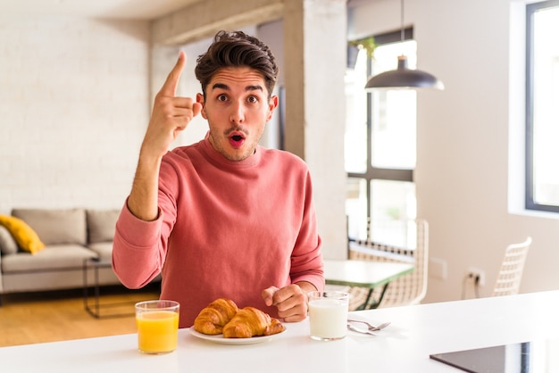 Homem jovem de raça mista tomando café da manhã em uma cozinha de manhã, tendo uma ideia, o conceito de inspiração.