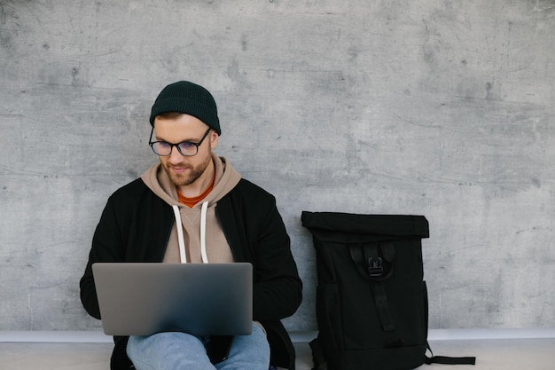 Homem jovem desenvolvedor de software usando computador portátil escrevendo código de programação enquanto está sentado no chão no escritório moderno de inicialização criativa