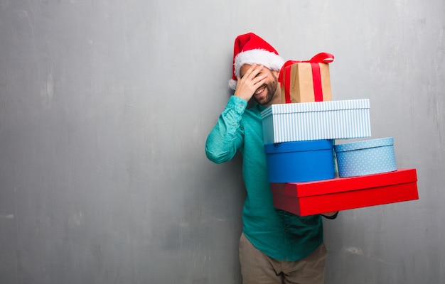 Homem jovem, desgastar, um, chapéu santa, presentes prendendo, envergonhado, e, rir, ao mesmo tempo