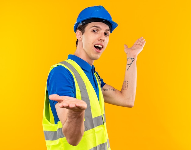 Homem jovem e alegre construtor de uniforme espalhando as mãos