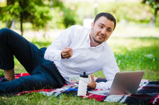 Homem jovem e atraente relaxa no parque na hora do almoço
